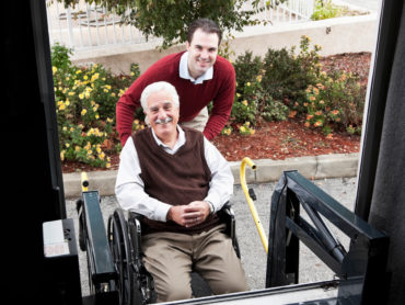 Male helping Male in Wheelchair get into a vehicle