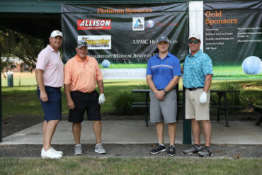four golfers standing with sponsorship banner